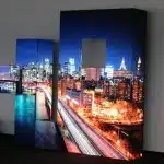Large LEDCON SL-3.75SI 3.75mm Ecke 90° LED wall modules display a vibrant night cityscape with colorful traffic light trails against a plain wall; two rental LED panels feature square cutouts, creating visible gaps in the seamless city image.