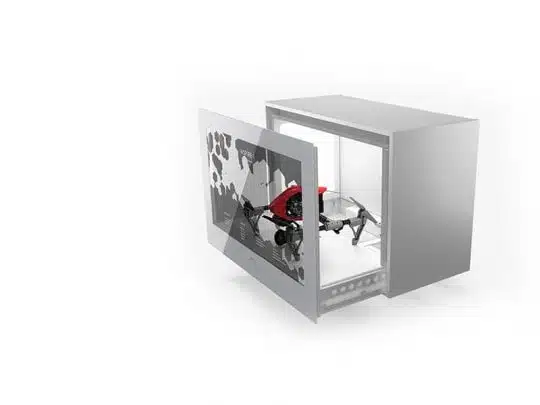 A small black and red drone displayed inside a sleek silver 43 Zoll Full HD Hypebox Touch (model HBT43L-WM) cabinet, with the transparent front door open, showcasing the drone against a clean white background.