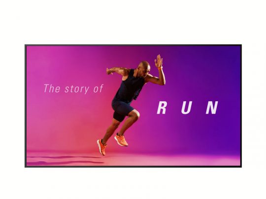 A man in athletic wear runs across a vibrant pink and purple gradient background displayed on the large 110-inch Digital Signage Display - LG 110UM5J-B. Bold white text overlay says The story of RUN. The screen showcases vivid colors and crisp details, ideal for dynamic advertising or event promotion.