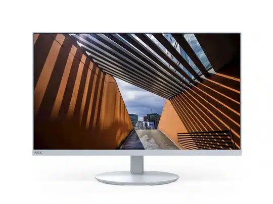 White-framed computer monitor displaying a vivid photo of an outdoor walkway with orange walls and metal slats casting striped shadows, leading to a distant cityscape beneath a cloudy sky.