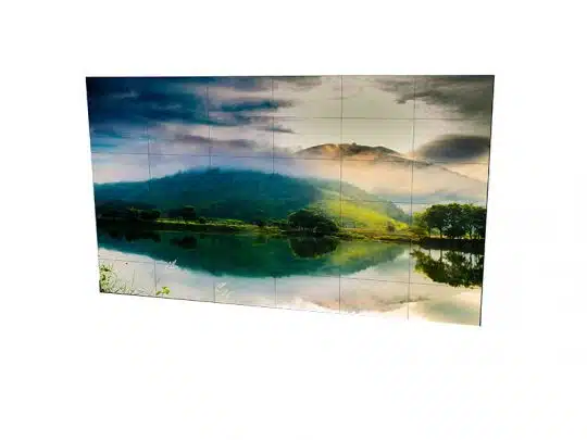 Steglose Videowand 6x6 aus 55 Zoll Displays mieten - Das Produktbild zeigt eine moderne, randlose Videowand bestehend aus 36 nahtlos aneinandergereihten Bildschirmen, auf denen ein Landschaftsmotiv mit ruhigem See, grünen Hügeln und Sonnenlicht unter bewölktem Himmel angezeigt wird. Optimal für Events und Präsentationen.