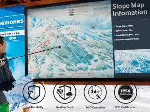 Eine Person in Skibekleidung zeigt auf eine große Pistenkarte, die auf dem 75 Zoll Outdoor LCD Display - Samsung OH75F angezeigt wird; das wetterfeste und robuste Display eignet sich ideal für den Einsatz im Außenbereich und kann rund um die Uhr betrieben werden (IP56-zertifiziert).