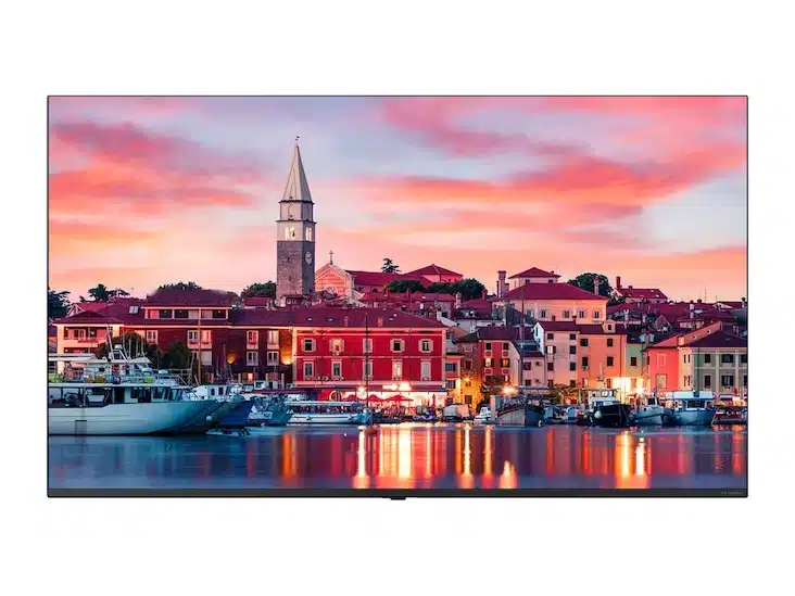 Wasserfront-Stadt mit bunten Häusern, Booten im Yachthafen und einer Kirche mit hohem Turm vor einem leuchtenden Sonnenuntergang mit pink-orangenen Wolken - Immobilien in attraktiver Lage am Wasser zum Kaufen oder Mieten.