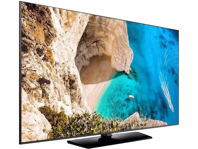 Flachbildfernseher, wahlweise zum Mieten oder Kaufen, zeigt auf dem Display eine Luftaufnahme einer sandigen Bucht mit türkisfarbenem Wasser, Klippen, viel Grün und mehreren Booten; das Gerät hat einen dünnen Rahmen und einen schwarzen Standfuß.