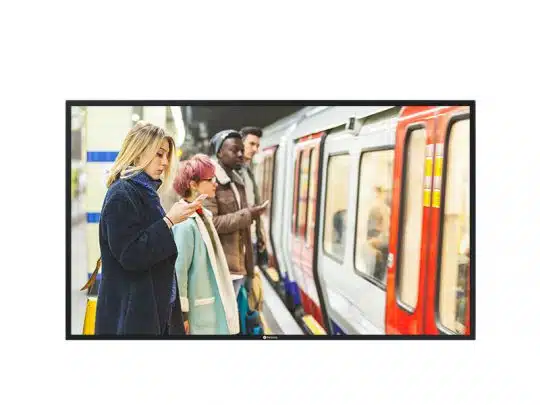 Vier Personen stehen nebeneinander auf einem U-Bahnsteig in einer modernen, urbanen U-Bahnstation und warten auf einen haltenden Zug. Im Vordergrund blickt eine Frau konzentriert auf ihr Smartphone, vermutlich auf der Suche nach Angeboten zum Kaufen oder Mieten, während die anderen entspannt hinter ihr warten. Das Bild vermittelt typische Alltagssituationen beim Pendeln in der Stadt und unterstreicht die Nutzung mobiler Geräte zur Immobiliensuche unterwegs.