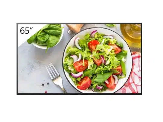 65-Zoll-Fernseher Samsung QLED zeigt gestochen scharf ein Bild von frischem Salat mit Kopfsalat, Tomaten, roten Zwiebeln und Spinat in einer Schüssel. Im Vordergrund auf dem hellgrauen Tisch liegen eine Gabel, Olivenöl und eine Serviette - ideal für Kunden, die den Fernseher kaufen oder mieten möchten.