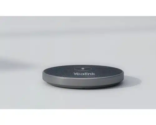 Drahtloses Mikrofon Yealink VCM36-W, neu und rundes flaches Design mit zentralem Knopf und Yealink-Logo, liegt auf hellgrauer Fläche - perfekt zum Kaufen oder Mieten für professionelle Konferenzen.