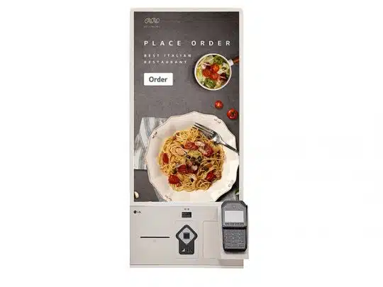 Selbstbedienungs-Bestellterminal mit Touchscreen, auf dem ein Menü mit Foto von Pasta und Salat sowie der Hinweis "Place Order" angezeigt wird; unterhalb des Bildschirms ist ein Kartenlesegerät für kontaktlose Bezahlung angebracht.