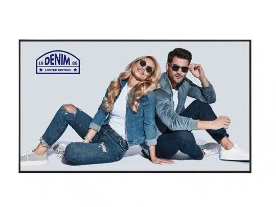 Ein Mann und eine Frau tragen lässige Denim-Mode - Jeansjacken, Jeanshosen und Sonnenbrillen - und sitzen nebeneinander auf dem Boden vor einem hellen Hintergrund. Im oberen linken Bildbereich ist das "Denim Limited Edition 1986"-Logo sichtbar.