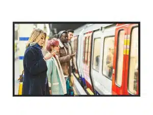 Mehrere Menschen stehen auf einem U-Bahnsteig und schauen auf ihre Smartphones, während eine U-Bahn mit bewegter Unschärfe einfährt. Die Szene ist belebt; die Pendler tragen Winterkleidung.