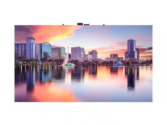 Sonnenuntergang über einer Stadt-Skyline, die sich in einem ruhigen See spiegelt; im Wasser steht ein Springbrunnen, im Hintergrund ragen moderne Hochhäuser empor und farbenfrohe Wolken ziehen am Himmel entlang.