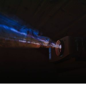 Beamer mieten in Nahaufnahme im dunklen Raum: Der Projektor strahlt leuchtende blaue und violette Lichtstrahlen aus.