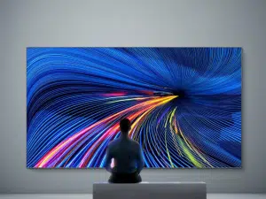 The View - LED Wand 130 Zoll Full HD" an der Wand zeigt dynamische blaue Lichtlinien und Tunnel-Effekt, Person sitzt davor.
