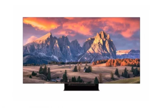 Der Samsung-Flachbildfernseher zeigt ein scharfes, farbenfrohes Bild mit Berggipfeln bei Sonnenuntergang, orangefarbenen Wolken, Bäumen, grünen Wiesen und kleinen Häusern im Vordergrund. Perfekt für realistische Fernseherlebnisse.
