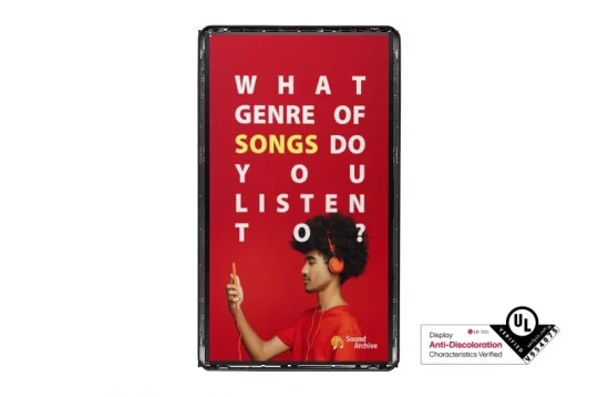 Produktbild: Eine Person mit roten Kopfhörern hält ein Smartphone in der Hand und zeigt nach oben. Im Hintergrund steht auf rotem Hintergrund: „WHAT GENRE OF SONGS DO YOU LISTEN TO?“, wobei das Wort „SONGS“ gelb hervorgehoben ist. Unten rechts befindet sich das UL-Zeichen gegen Verfärbung. Ideal für die Präsentation von Musik- oder Kopfhörerprodukten, benutzerfreundlich beschrieben für Menschen mit Sehbehinderungen.