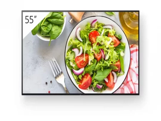 Ein 55-Zoll-Fernseher von Samsung zeigt eine Nahaufnahme eines frischen Salats; daneben liegen eine Gabel, eine Schüssel Spinat, Olivenöl und eine Serviette.