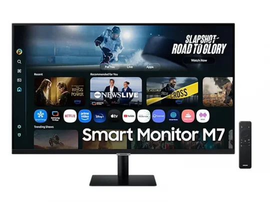 Der Samsung Smart Monitor M7 mit angezeigten Streaming-Apps und Empfehlungen auf dem Bildschirm; daneben steht eine Fernbedienung aufrecht.