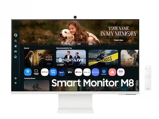 Samsung Smart Monitor M8 mit Streaming-Apps und Filmempfehlungen auf dem Bildschirm; oben ist ein Bild von einem Mädchen zu sehen, das einen Hund umarmt. Daneben liegt eine weiße Fernbedienung.