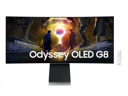 Der gebogene Samsung Odyssey OLED G8-Monitor steht auf einem Standfuß und zeigt eine farbenfrohe Science-Fiction-Szene. Rechts neben dem Monitor liegt eine Fernbedienung. Auf dem Bildschirm ist der Schriftzug „Odyssey OLED G8“ zu sehen.